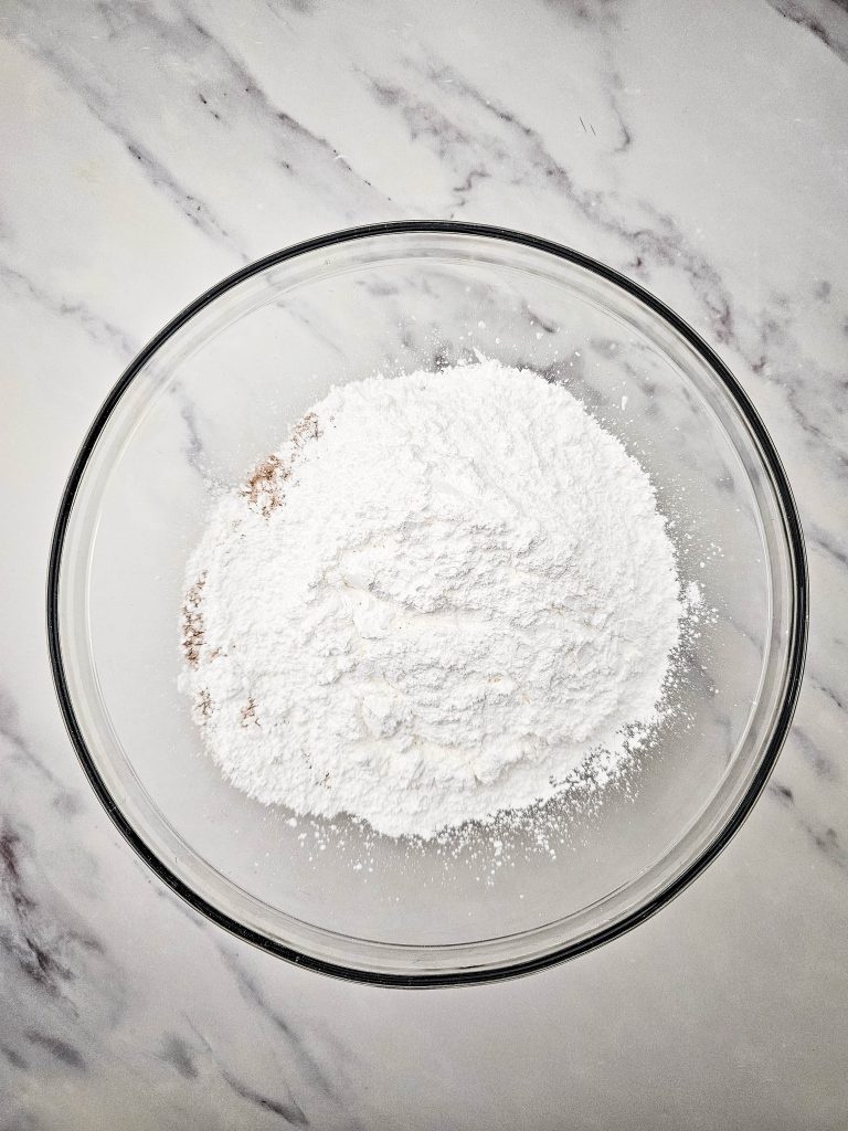 Powdered sugar added to red velvet cake mix in a mixing bowl.