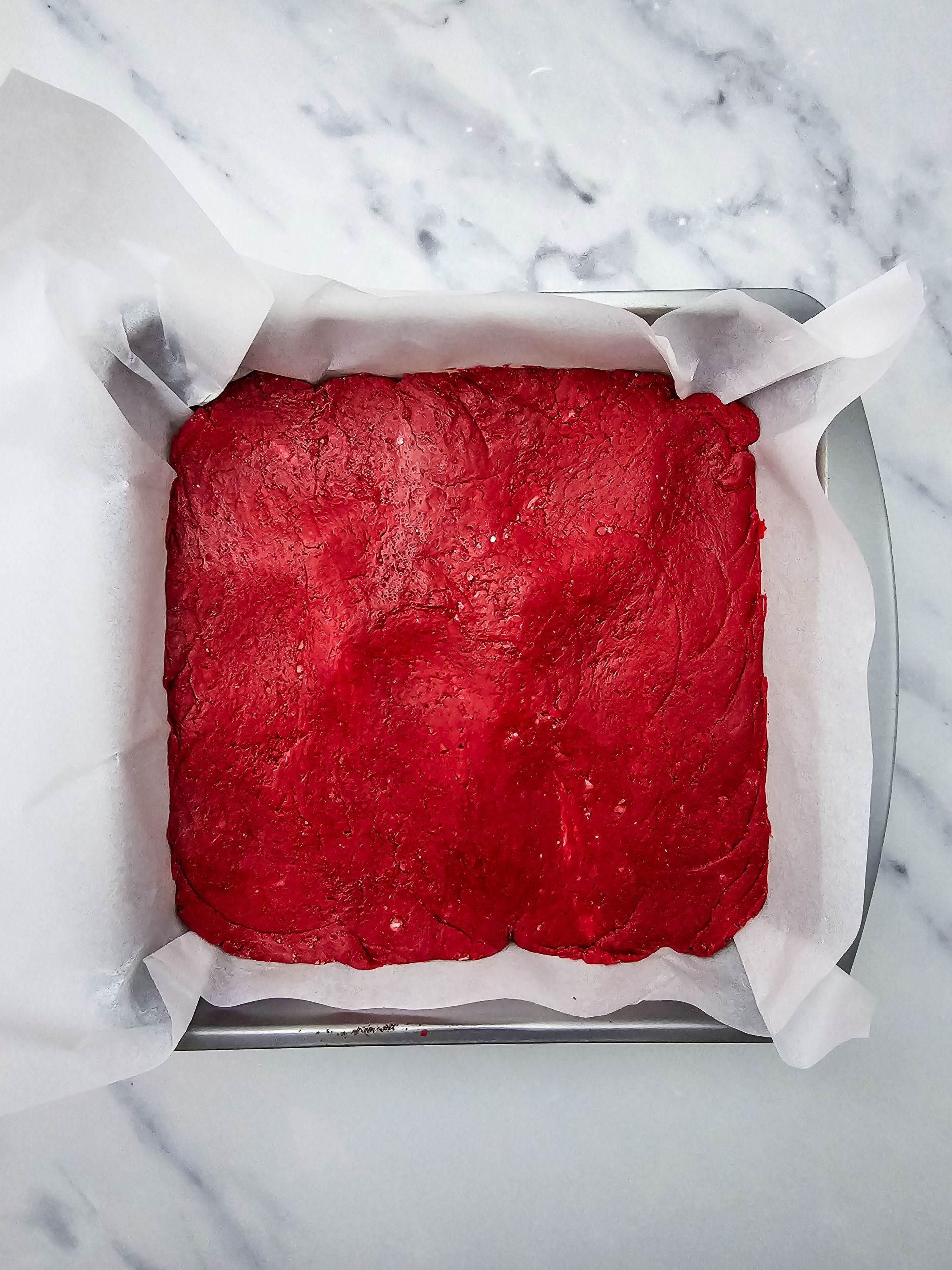 Red velvet fudge pressed evenly into a parchment lined pan.