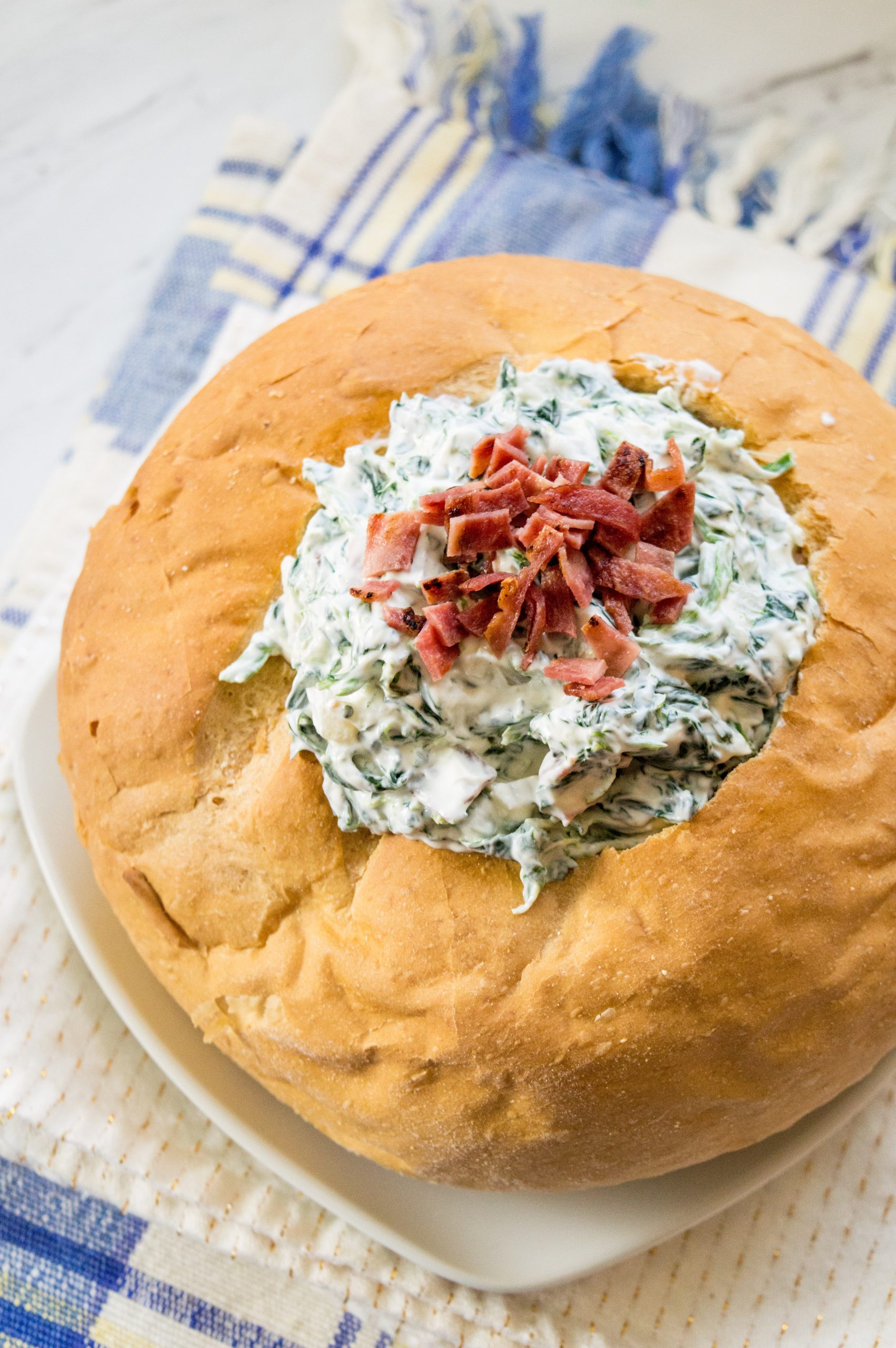 a bread bowl filled with Bacon Spinach Dip and topped with bacon.