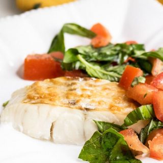 Parmesan Baked Haddock with Fresh Tomatoes and Basil on a white plate