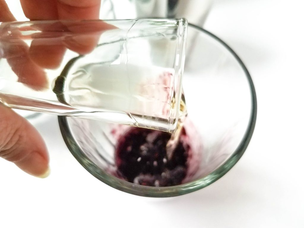 a shot being poured into a glass with blackberries
