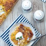 Rotisserie Chicken Enchilada Casserole in a white bowl, topped with sour cream and on a striped napkin