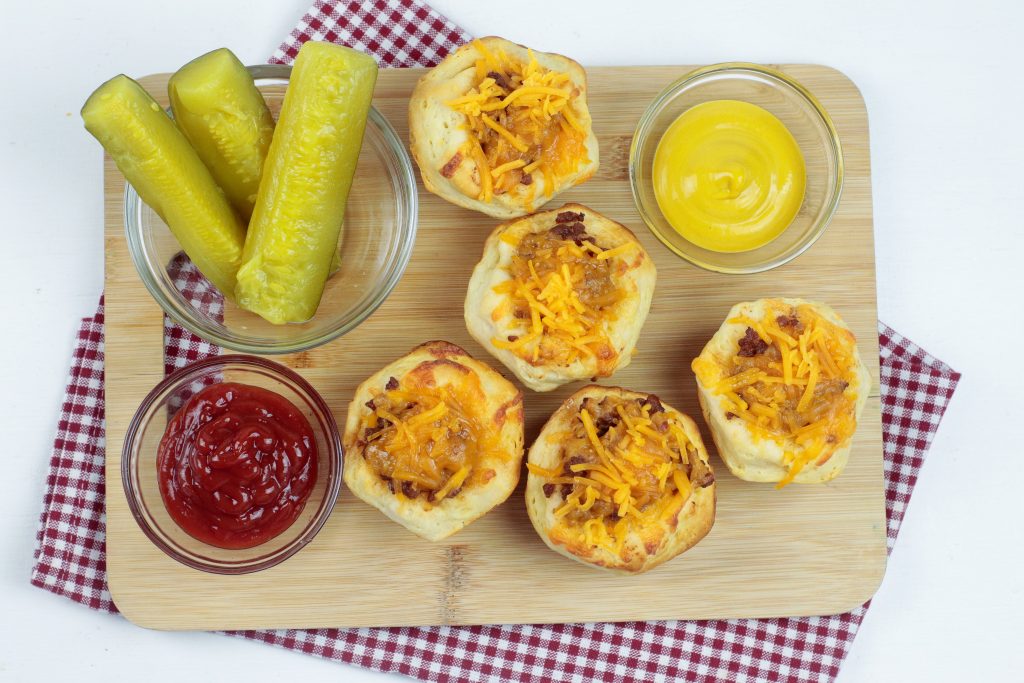 muffin cups on a wooden tray with pickles, ketchup and mustard