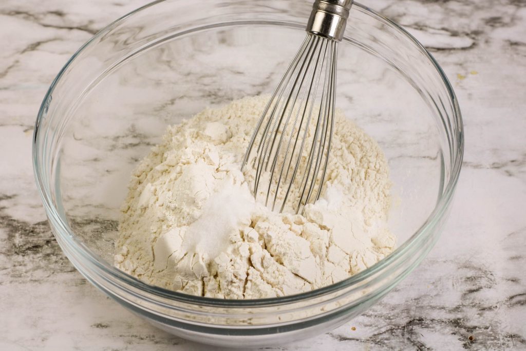 Flour, salt, and baking soda in a glass bowl with a whisk