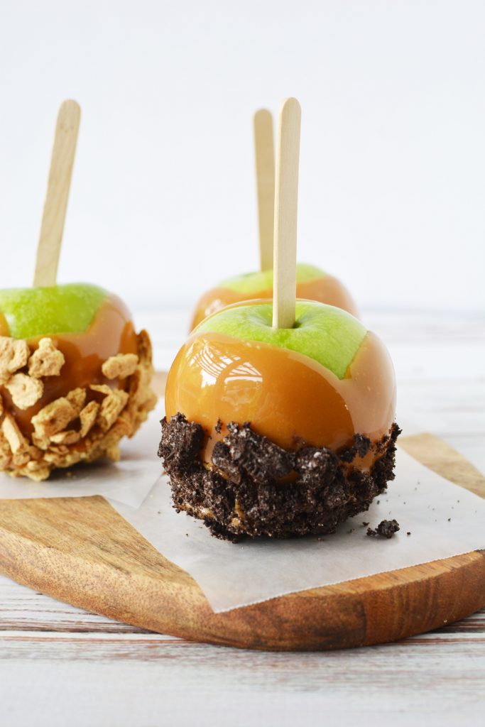Three Granny Smith apples dipped in caramel on a wooden circle