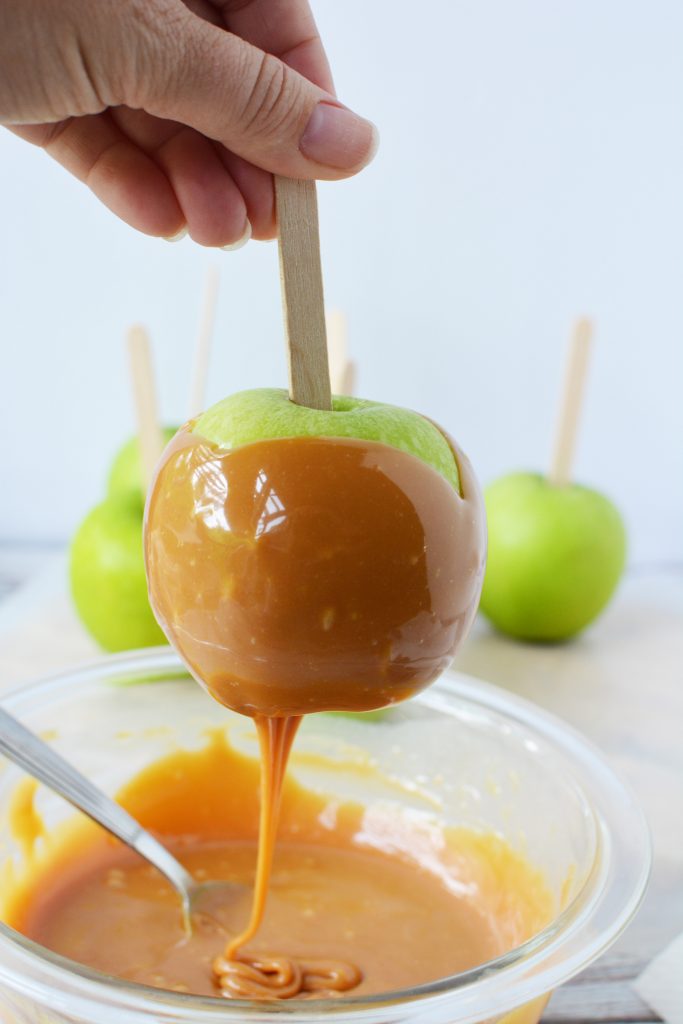 Pulling a Granny Smith apple that's been dipped in caramel out of the bowl