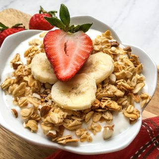 Homemade Greek Yogurt in a white bowl topped with granola, bananas and a strawberry