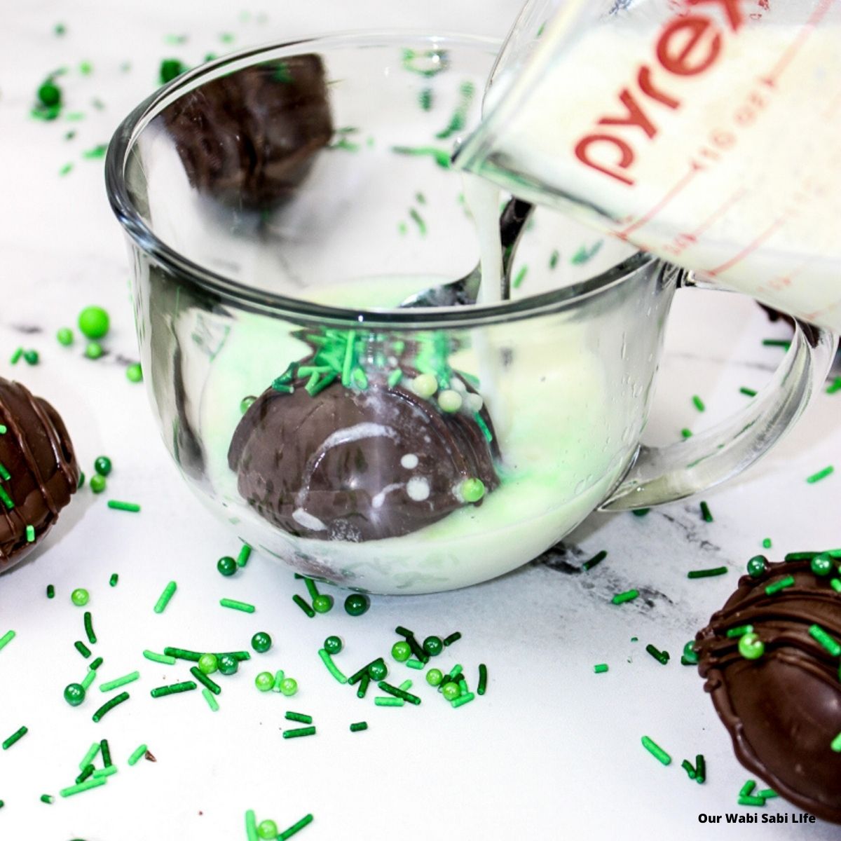 Pouring milk on top of a hot chocolate bomb with green sprinkles