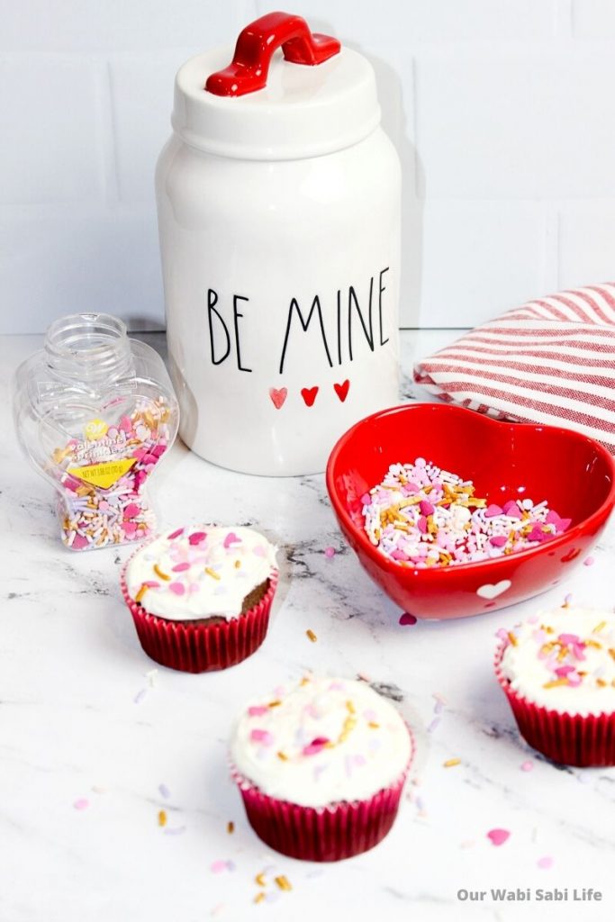 Valentine Sprinkle Cupcakes on a marble counter with a Be Mine Cookie Jar 