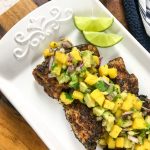 Four pieces of snapper seasoned with Cajun seasoning on a white tray and topped with salsa