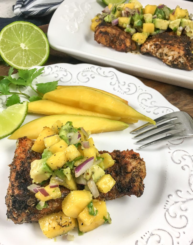 A piece of spicy Cajun snapper topped with Mango Avocado Salsa on a white plate