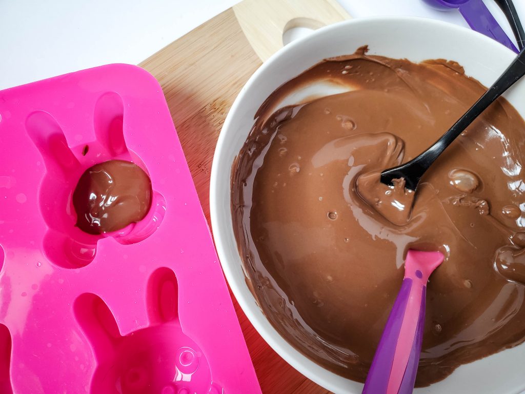 A bowl of melted chocolate next to a pink bunny face mold