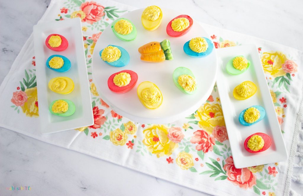 Two trays and a cake stand full of brightly colored deviled eggs