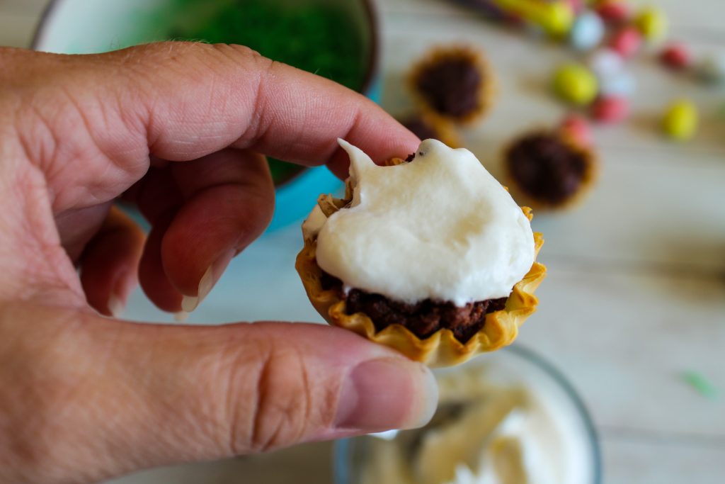 Adding cool whip onto of a brownie bite inside of a phyllo shell