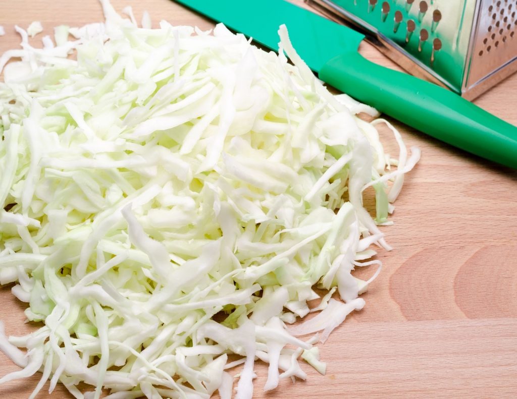 shredded cabbage on a cutting board with a green knife in the back