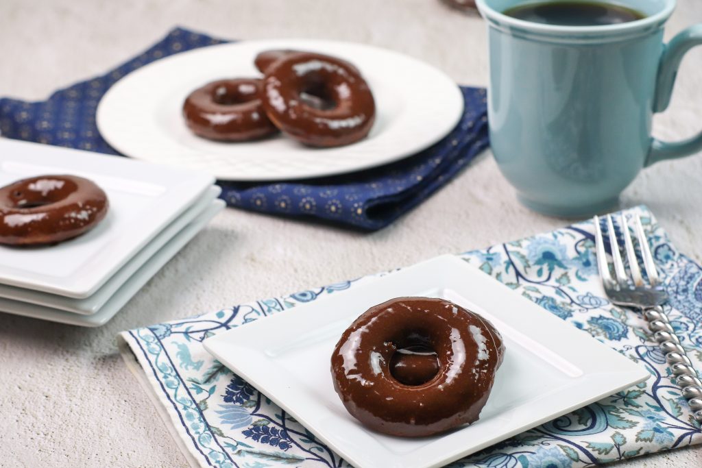 chocolate donut on a white plate with a coffee cup