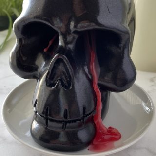 Black skull candle with red wax seeping out of eye socket.