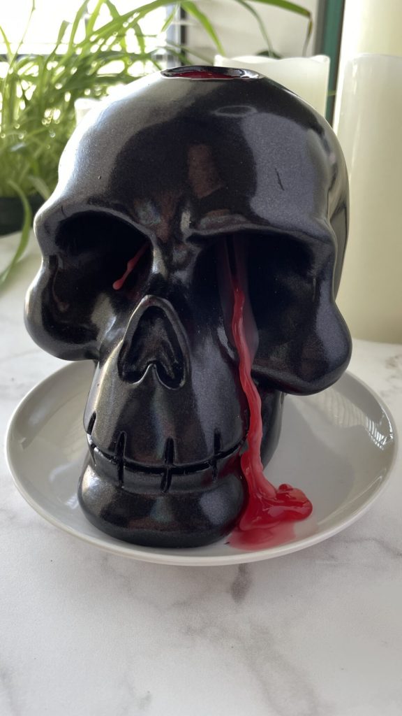Black skull candle with red wax seeping out of eye socket.