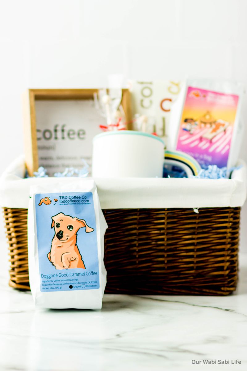 A bag of ground coffee sitting next to a basket with a coffee sign, mug, another bag of coffee.