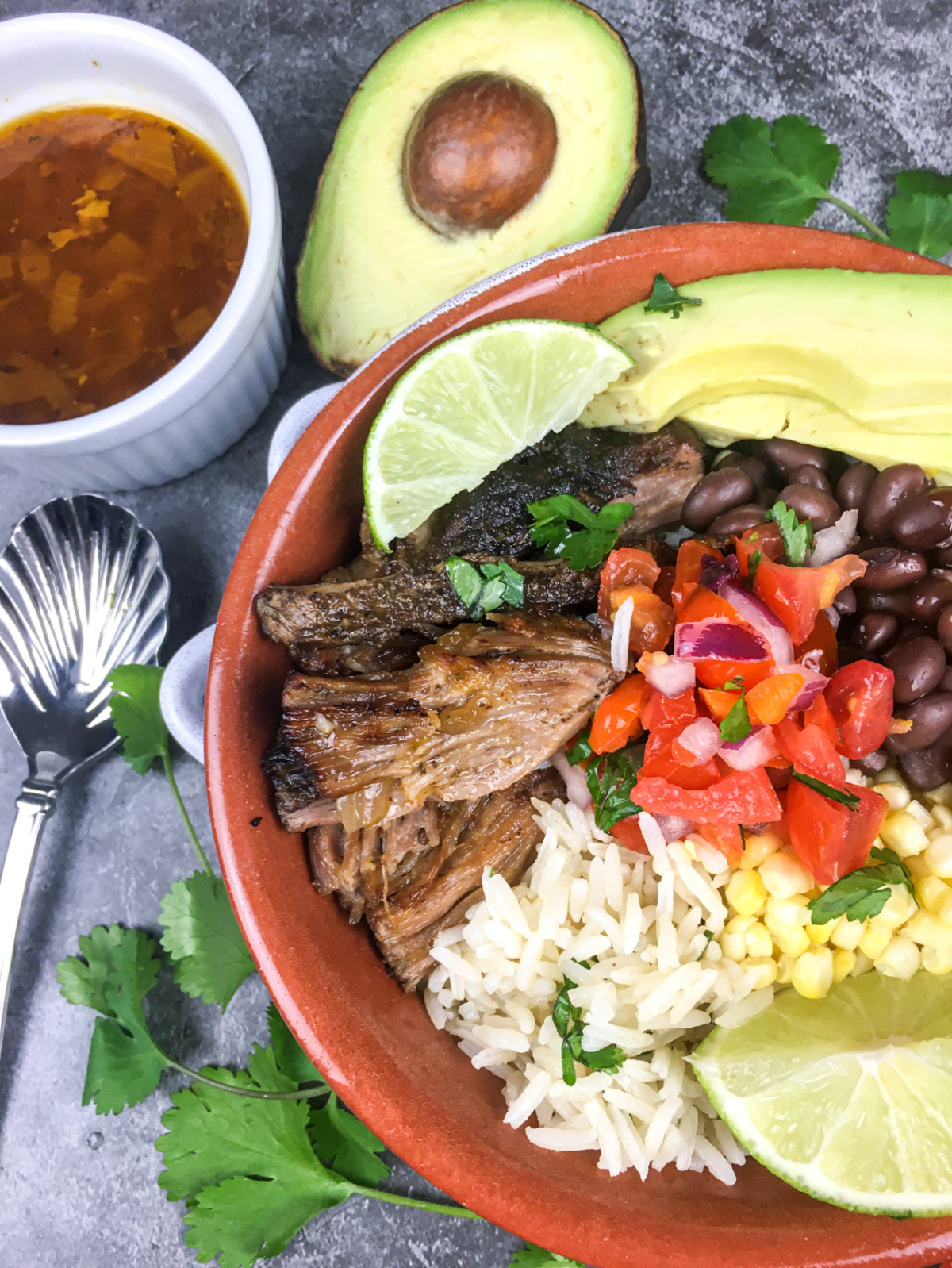 chipotle copycat carnitas in a reddish bowl with avocado and onions