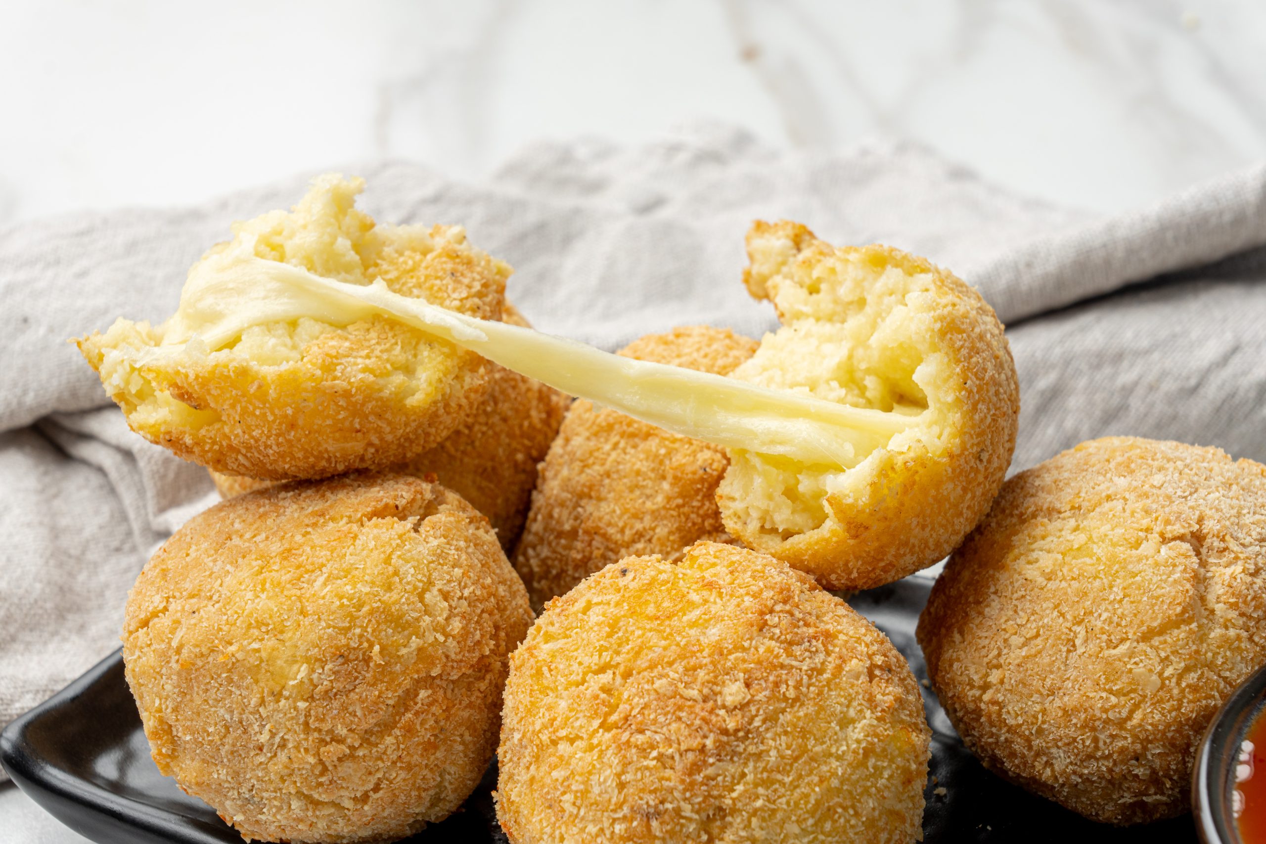 Golden brown potato cheese croquettes coated in breadcrumbs, served on a black plate