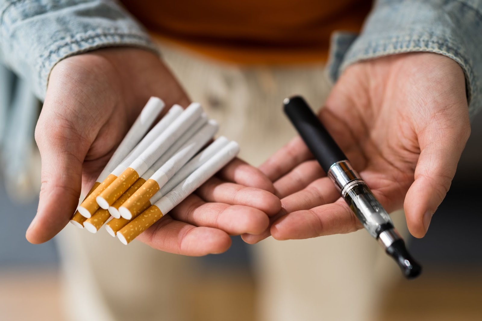 A man holds several cigarettes in one hand, and a vape device in the other