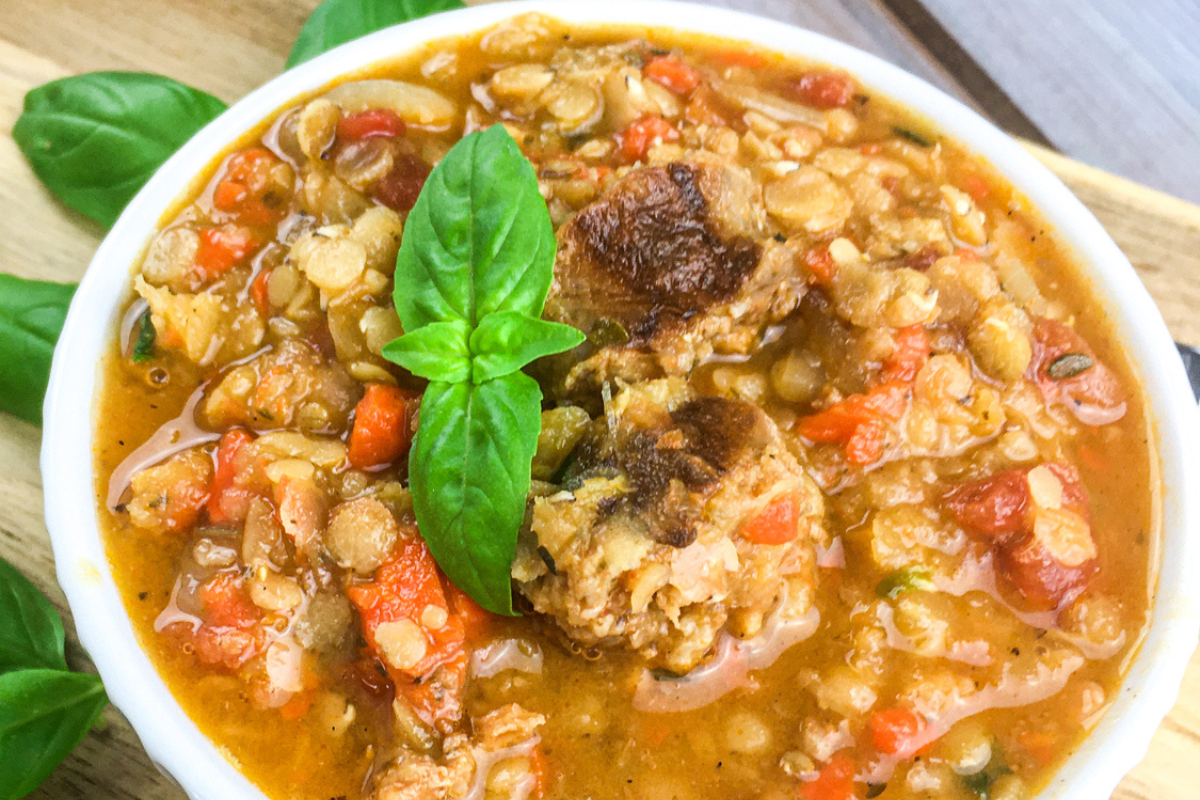 lentil and chorizo soup with basil garnish in white bowl