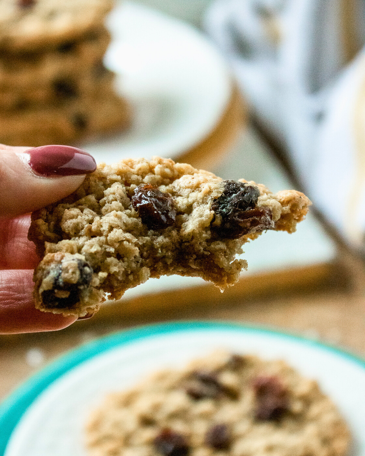 Hand holding a chewy oatmeal raisin cookie showing soft inside and raisins