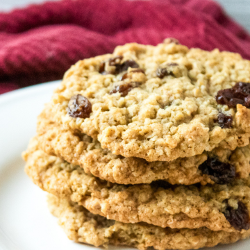 Close up of chewy oatmeal raisin cookies stacked on white plate with red towel