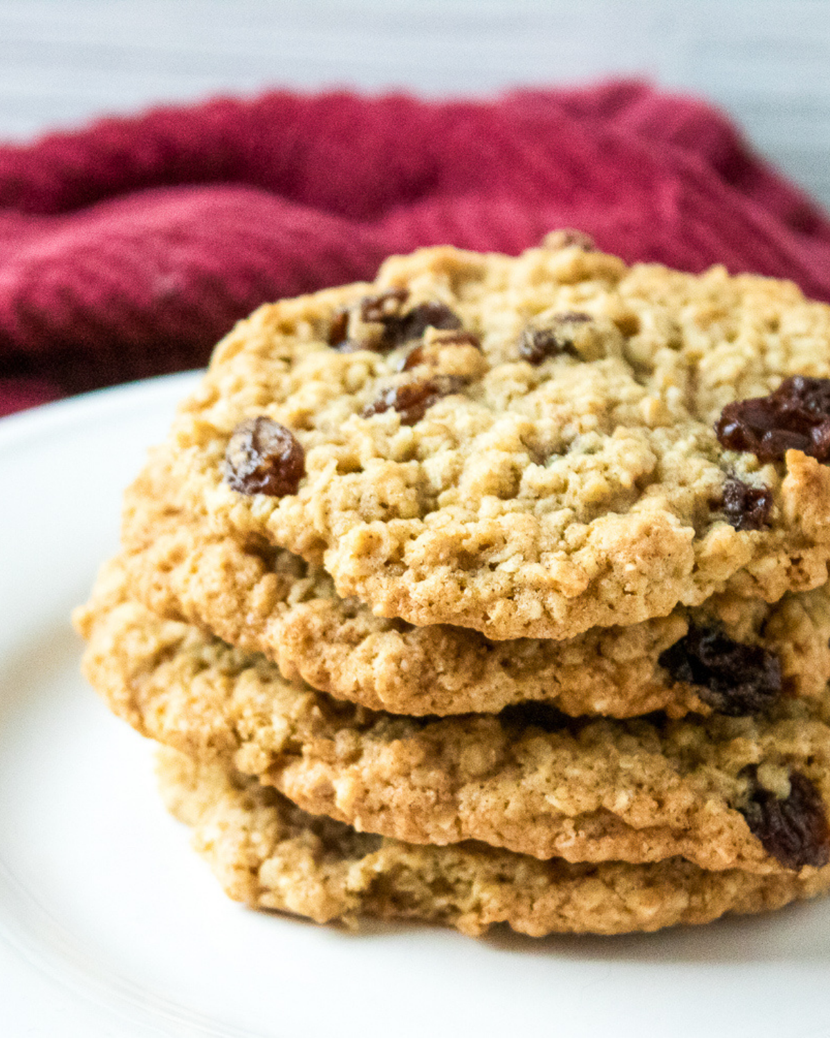 Close up of chewy oatmeal raisin cookies stacked on white plate with red towel