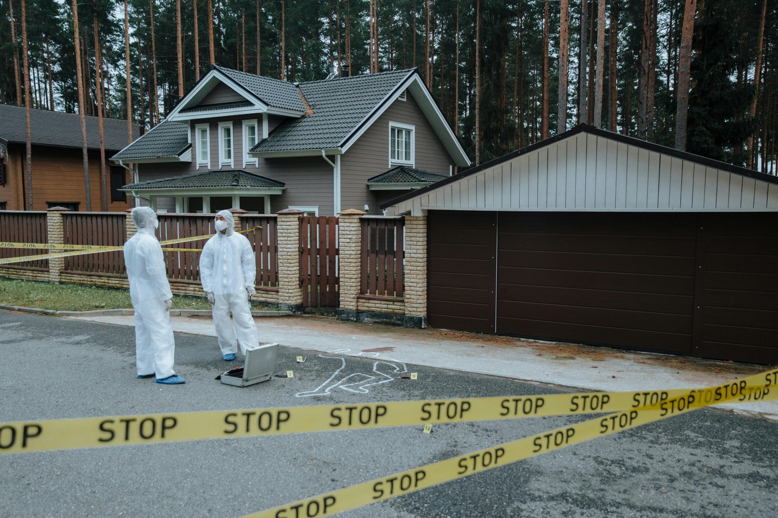 Crime scene investigators in protective suits examining evidence at a suburban house with yellow tape.
