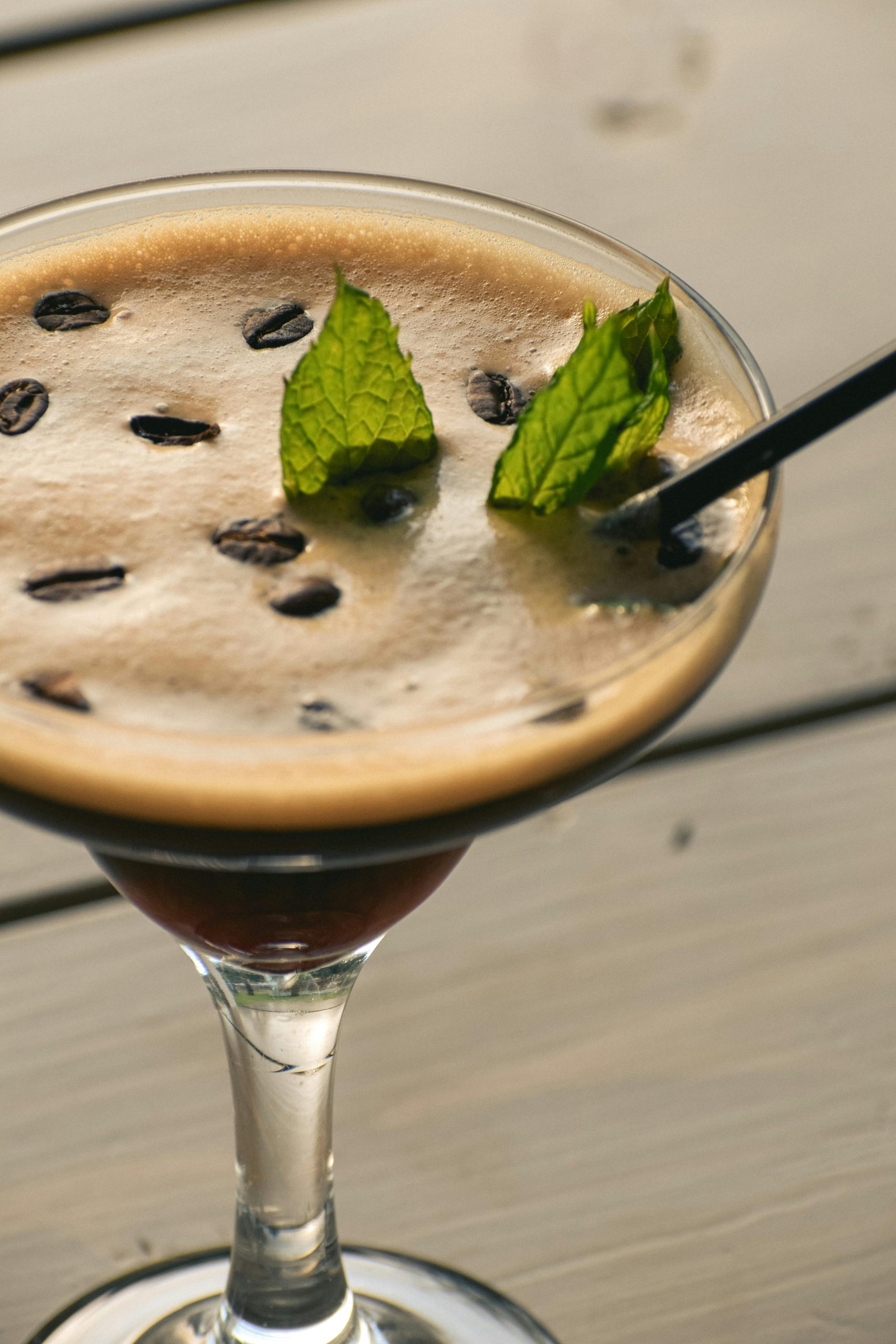A close-up of a creamy espresso martini topped with mint leaves and coffee beans.