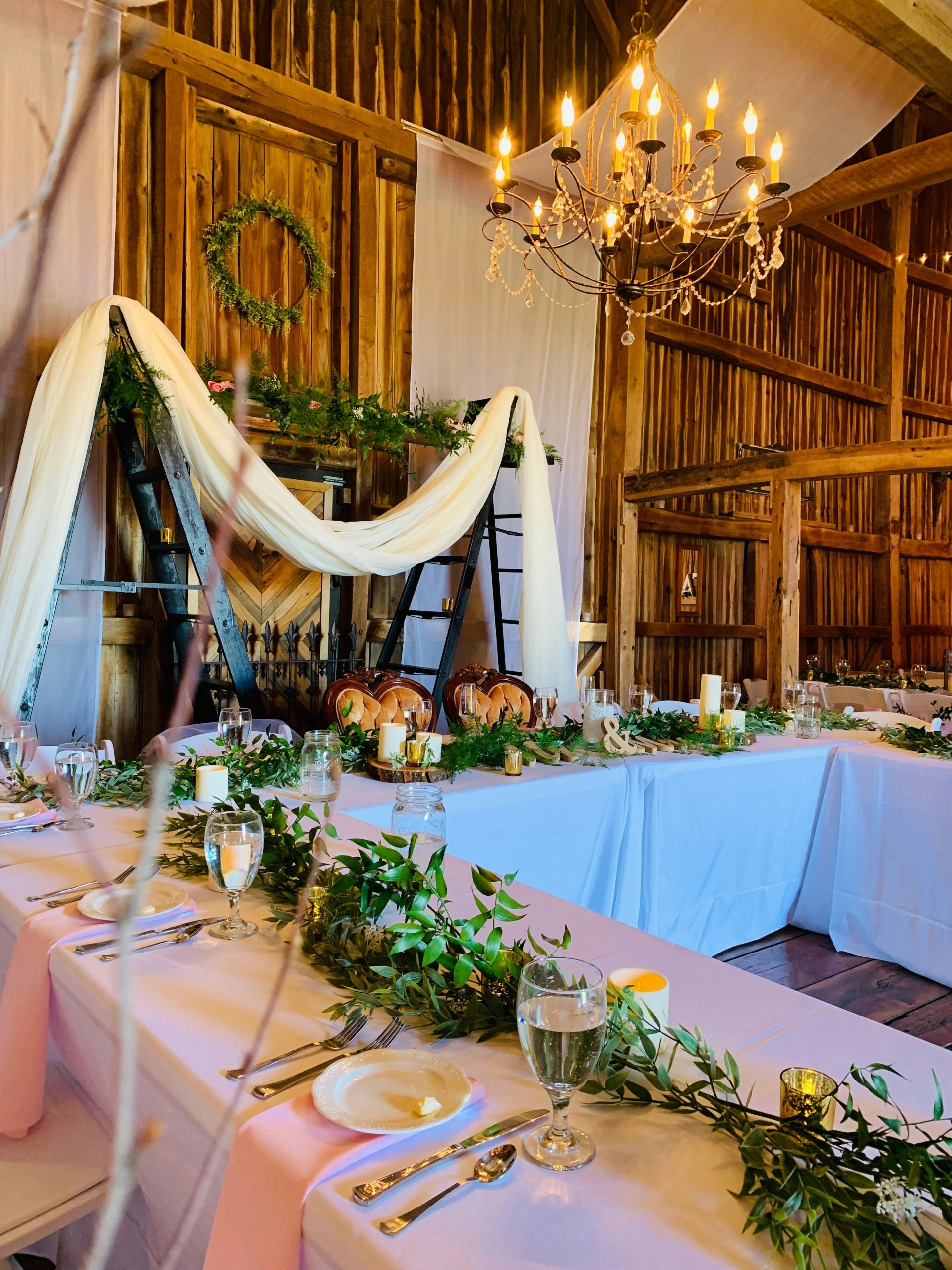 A beautifully set rustic wedding reception table indoors, featuring a chandelier and elegant decor.