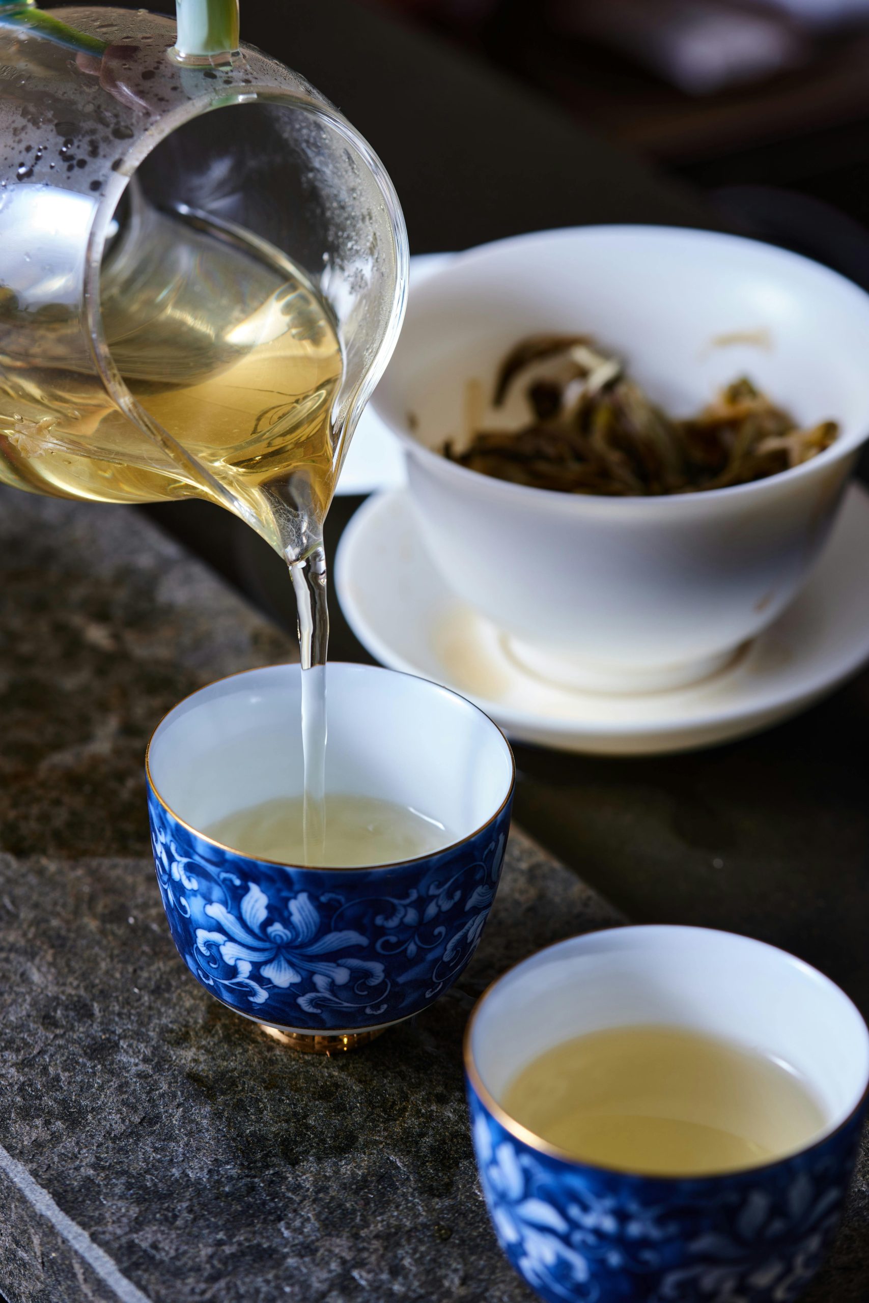 Delicately pouring tea from a glass pitcher into elegant blue porcelain cups. Still life capture.