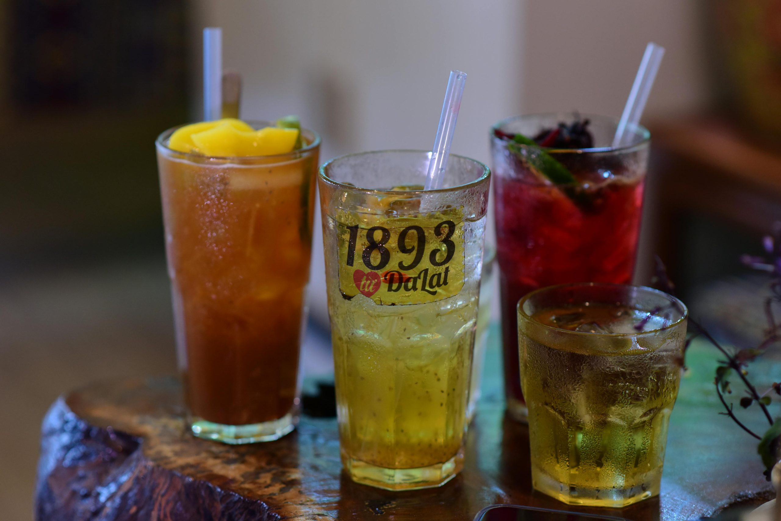 A variety of colorful iced drinks served in glasses with straws on a rustic table indoors.
