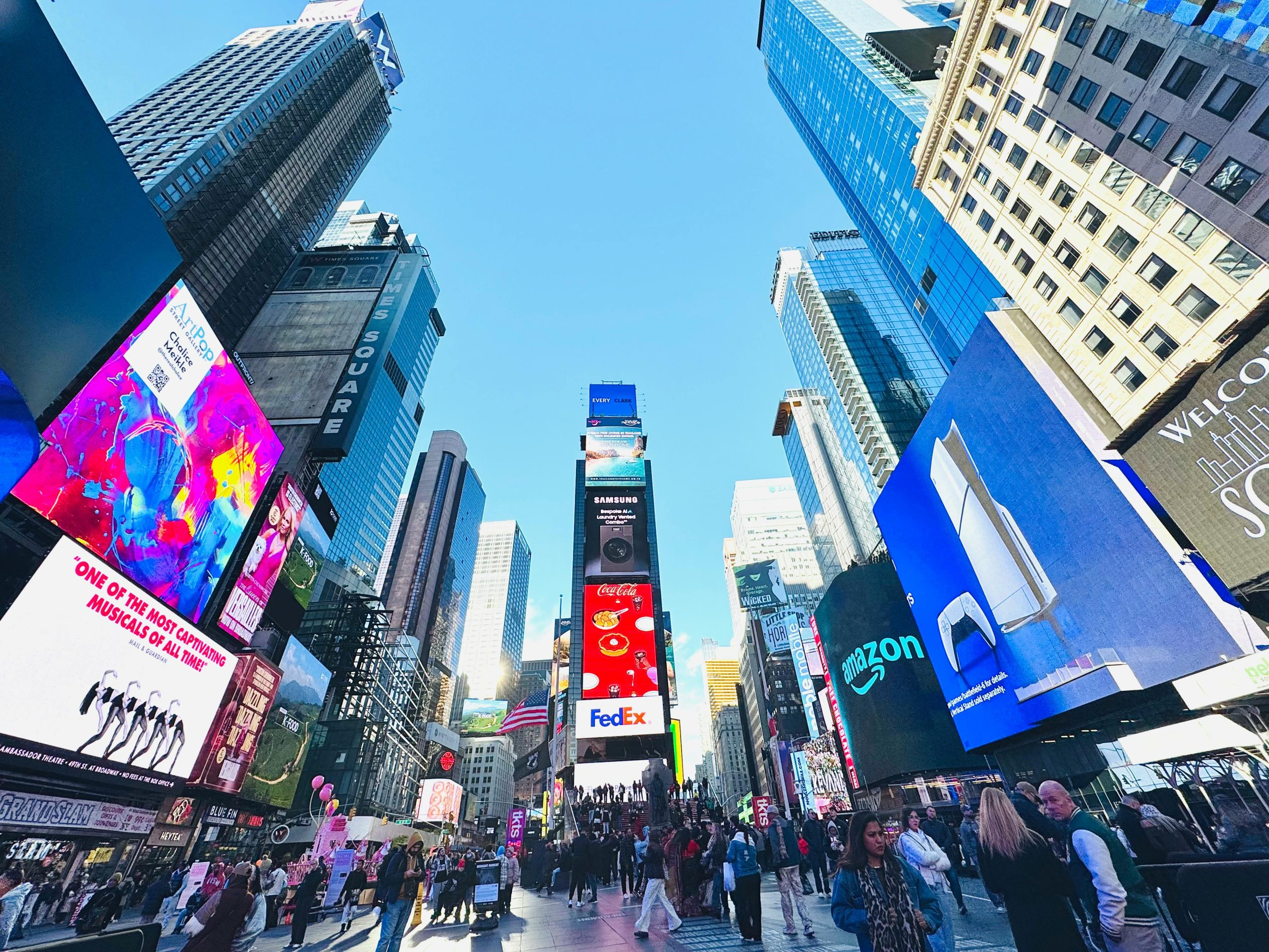 Vibrant daytime view of Times Square, showcasing iconic billboards and bustling crowd in New York City.