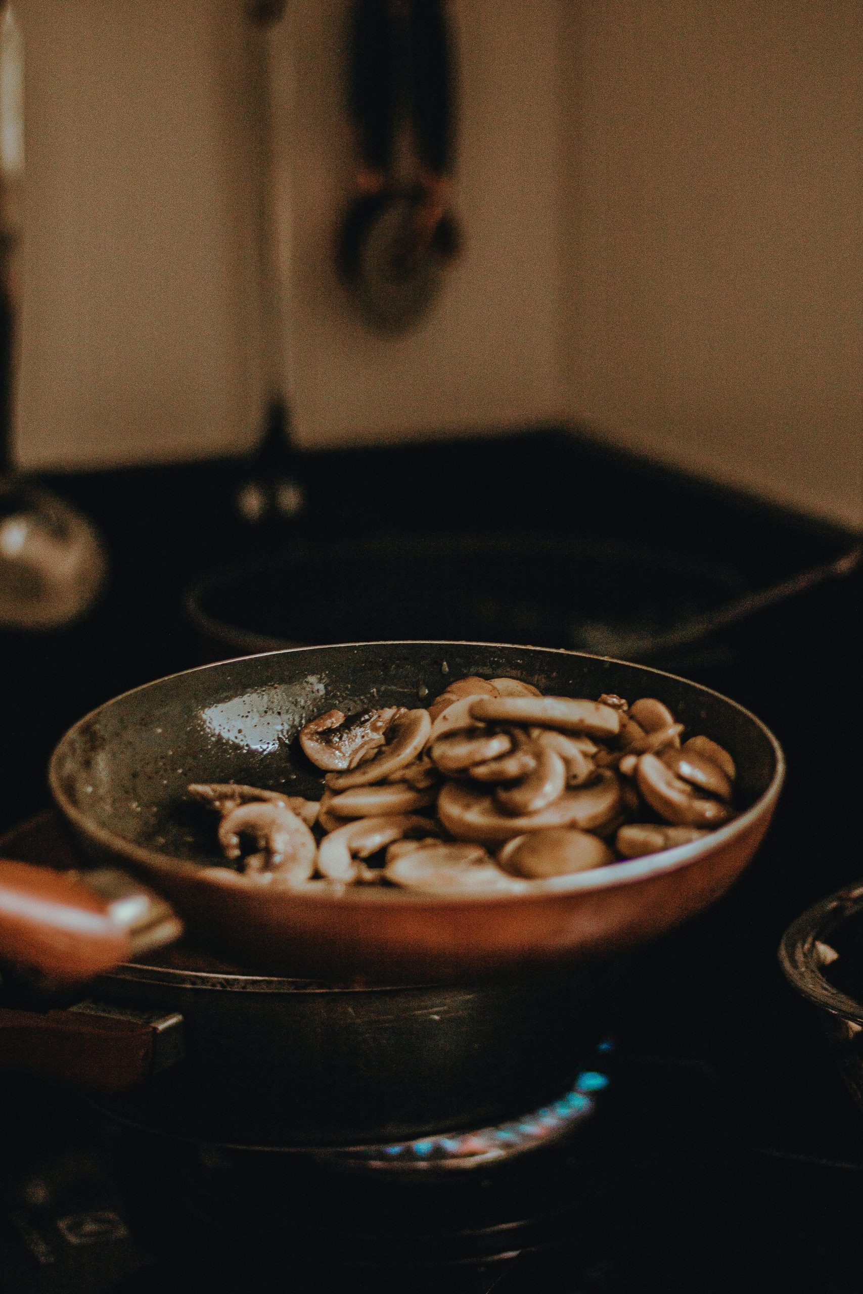 Delicious sliced mushrooms being sautéed in a frying pan on a stove.