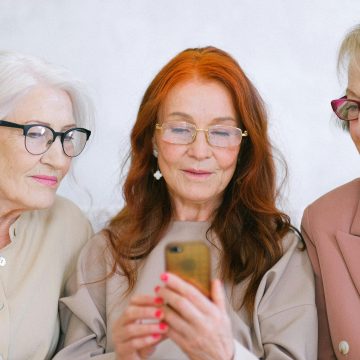 Group of elderly fashionable elegant women surfing internet on mobile phone together