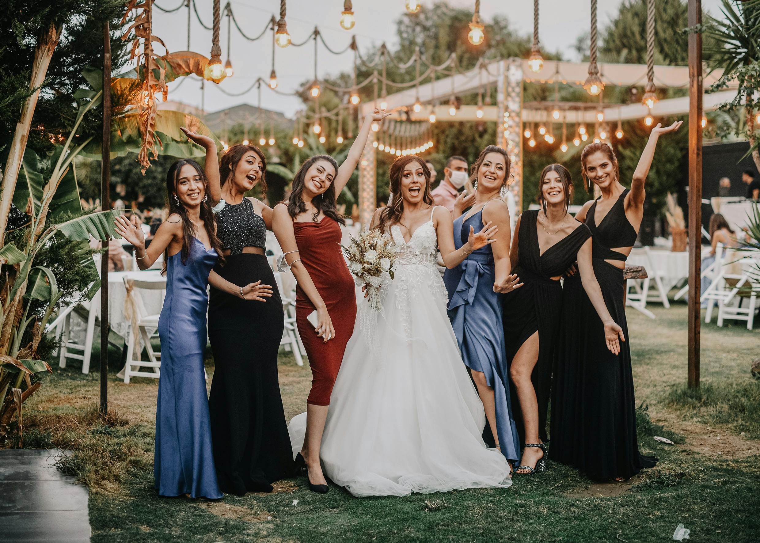 A joyful bridal party poses outdoors with festive lighting at a charming wedding venue.