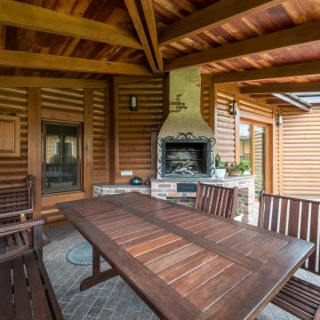Wooden table and benches in terrace with fireplace under roof near building in daytime