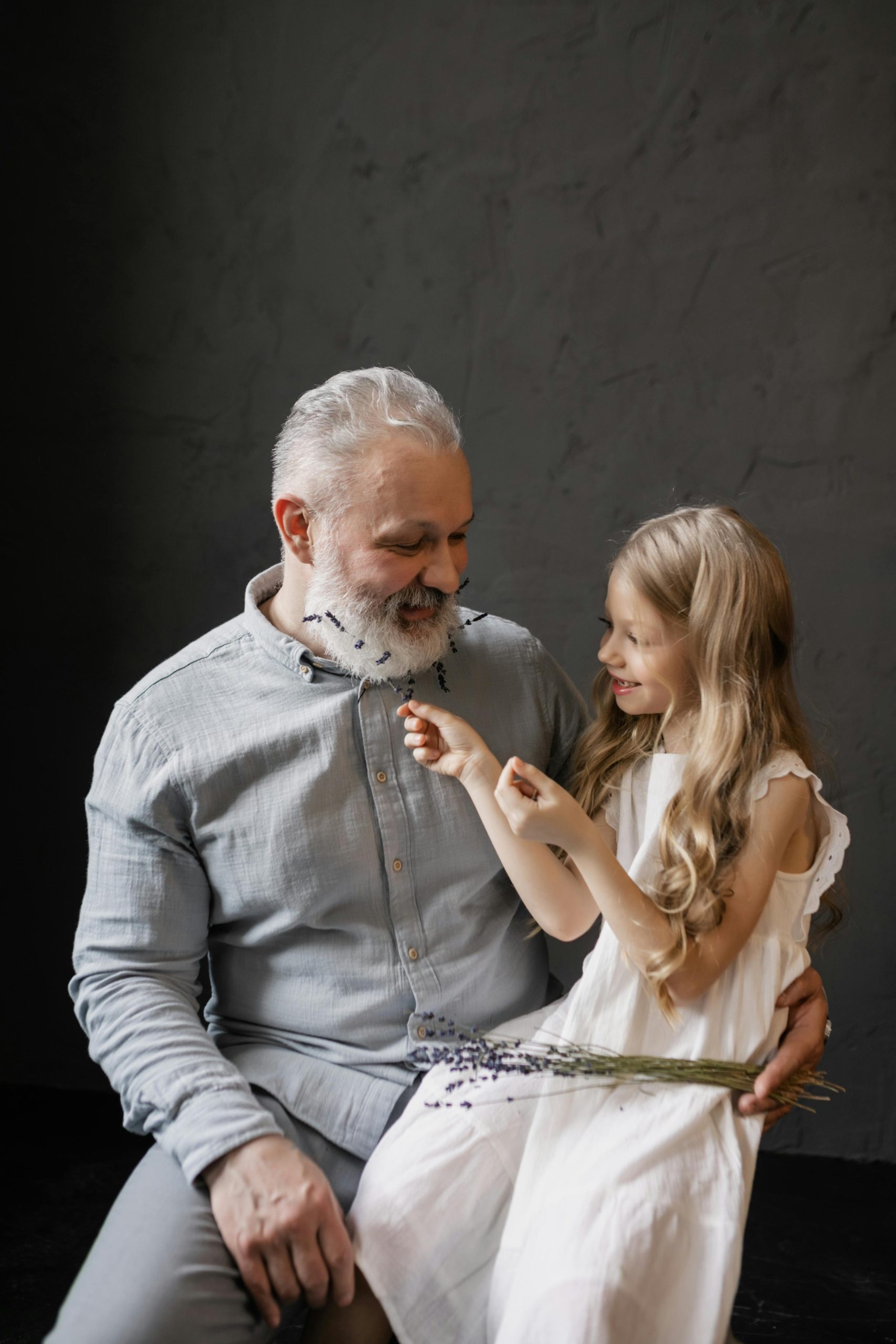 Smiling grandfather and granddaughter bonding together while holding flowers indoors.