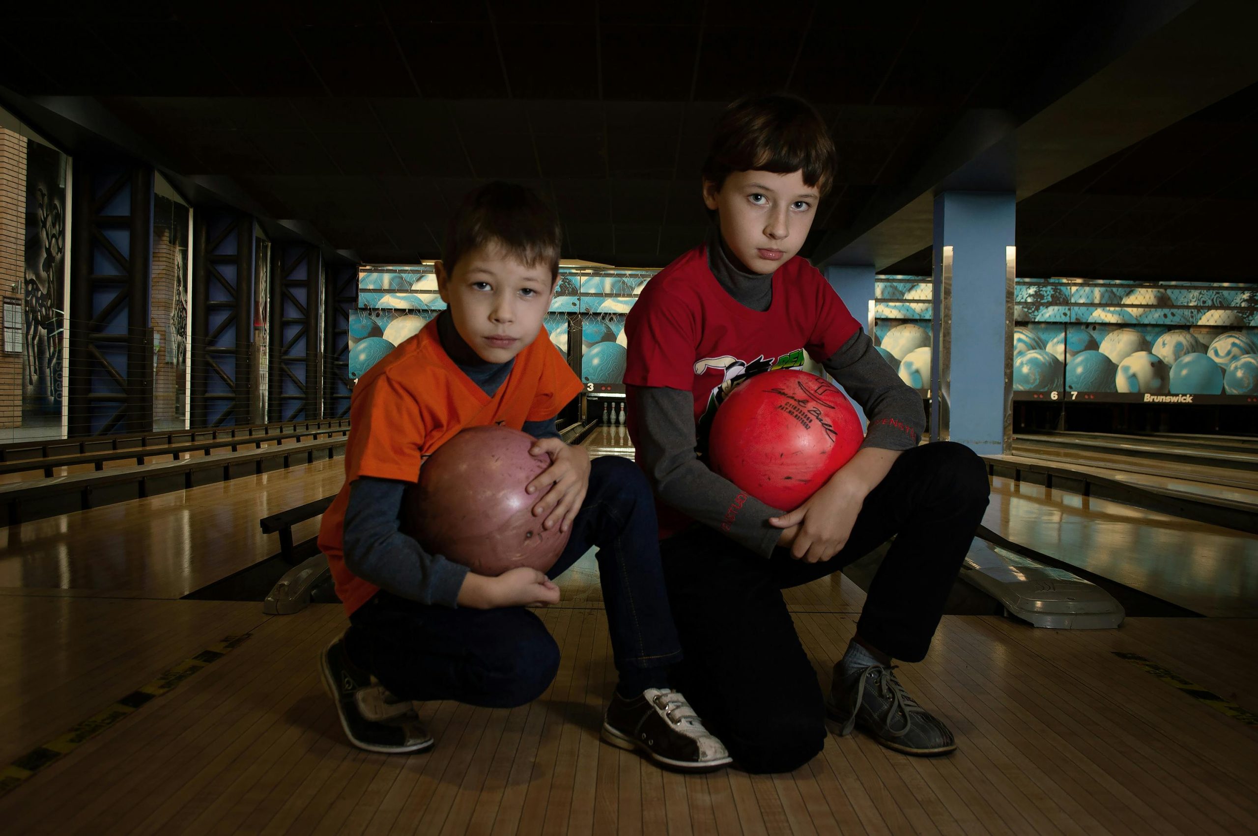 Two young boys with bowling balls at an indoor bowling alley.