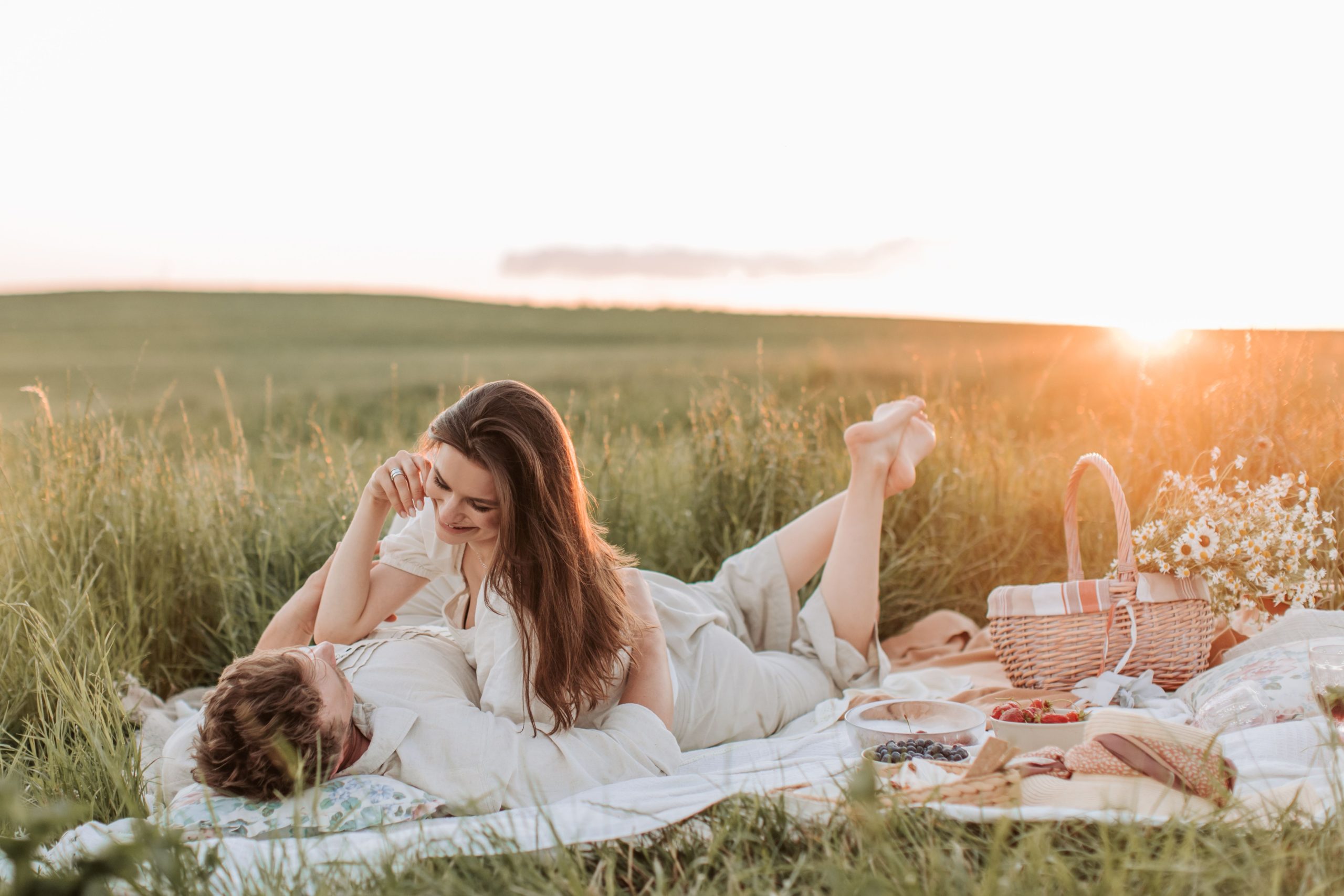 Couple enjoying a romantic picnic at sunset in a serene field.