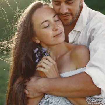 A loving couple embraces in a sunlit outdoor setting, enjoying a serene connection.