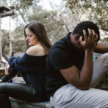 A couple sits back to back on a bench, depicting emotional conflict and loneliness.