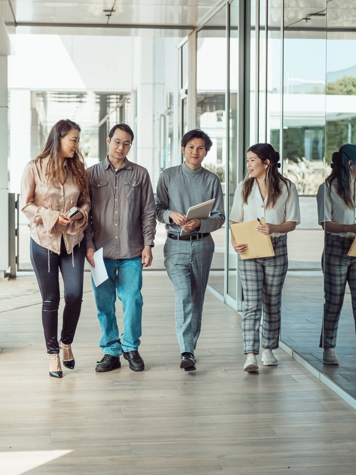 Group of four diverse colleagues walking outdoors, discussing work and holding documents.