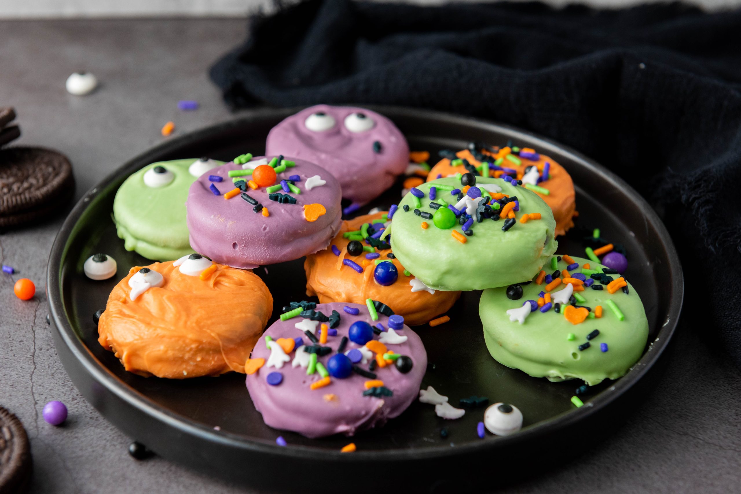 Halloween Oreos dipped in orange, purple, and green candy coating and topped with spooky candy eyes and colorful Halloween sprinkles.