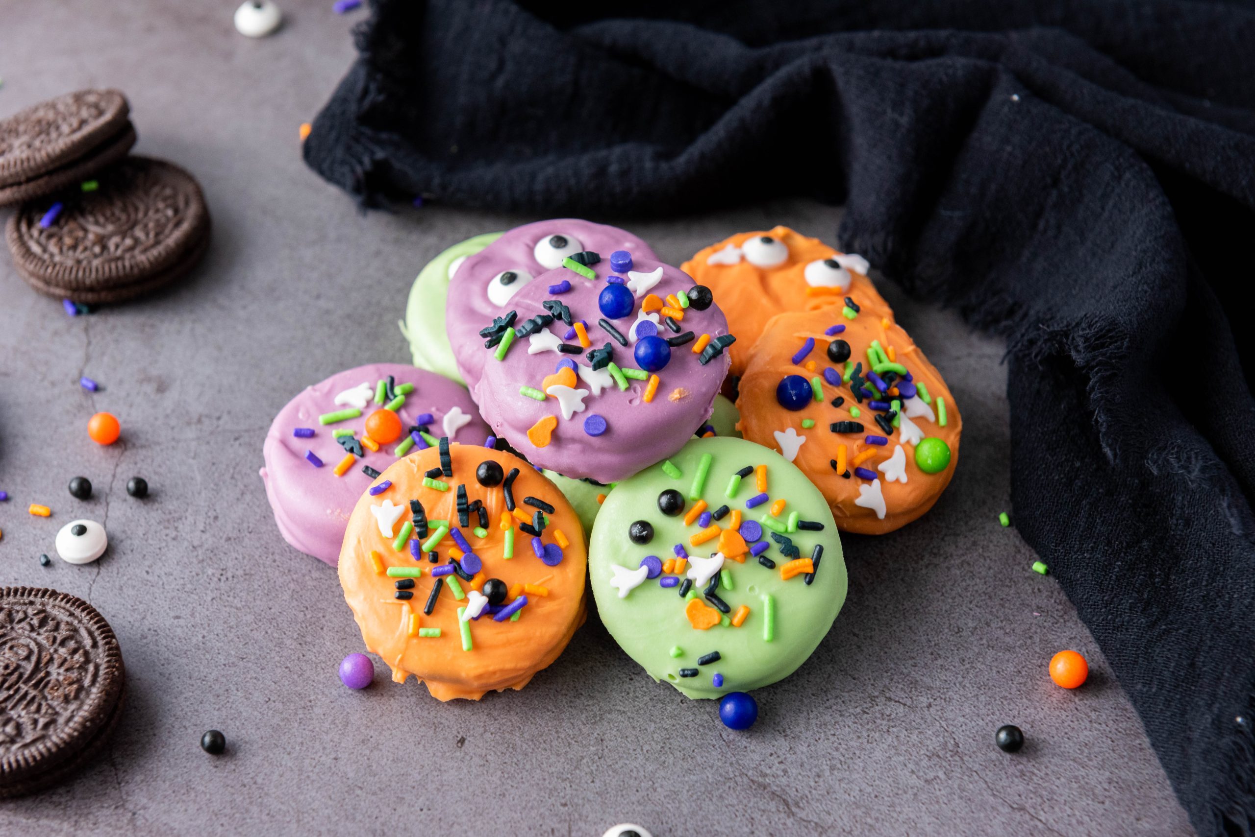 Halloween Oreos covered in colorful candy melts and decorated with spooky candy eyes and festive sprinkles for an easy Halloween dessert.