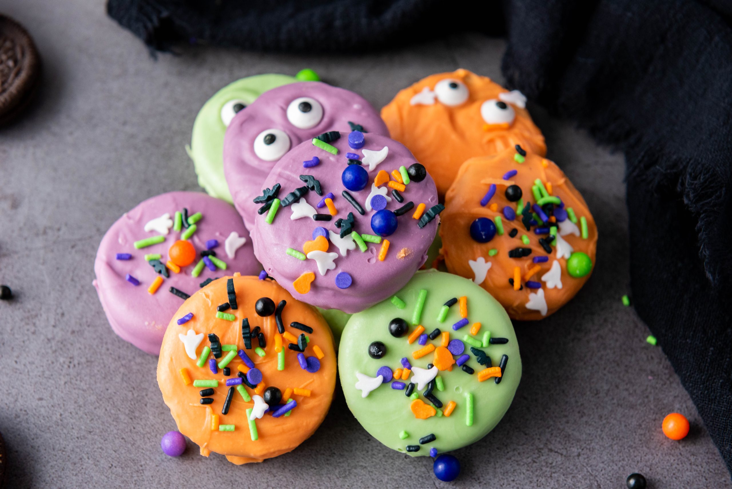 Halloween Oreos dipped in colorful candy coating and decorated with spooky candy eyes and festive Halloween sprinkles.