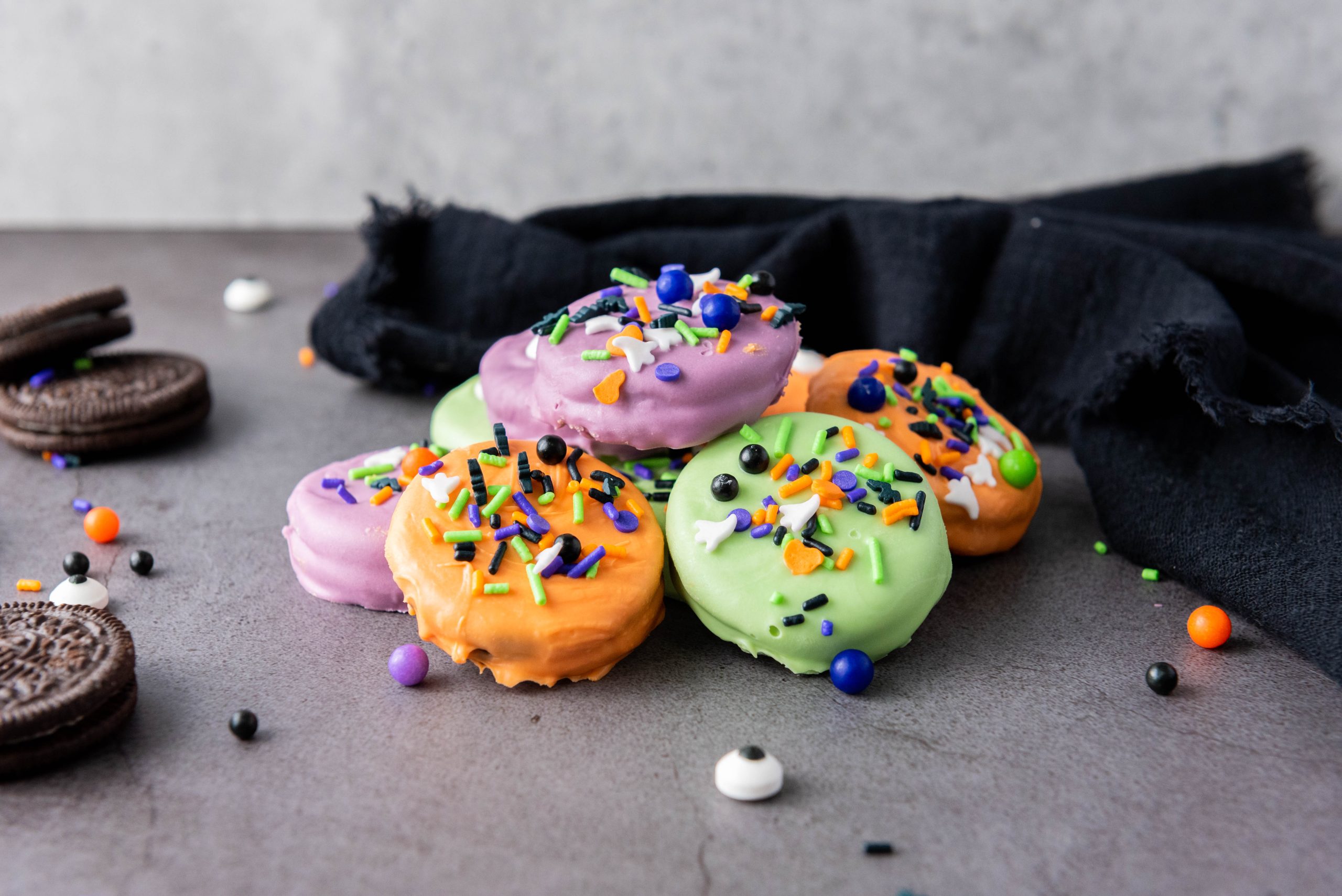 Colorful Halloween Oreos dipped in orange, purple, and green candy melts and decorated with candy eyes and festive sprinkles.